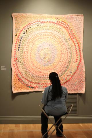 A woman sitting in front of a quilted artwork.