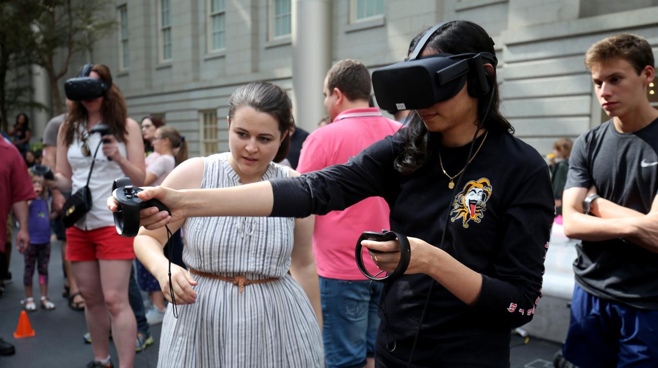 A photograph of a female playing a VR game with people watching. 