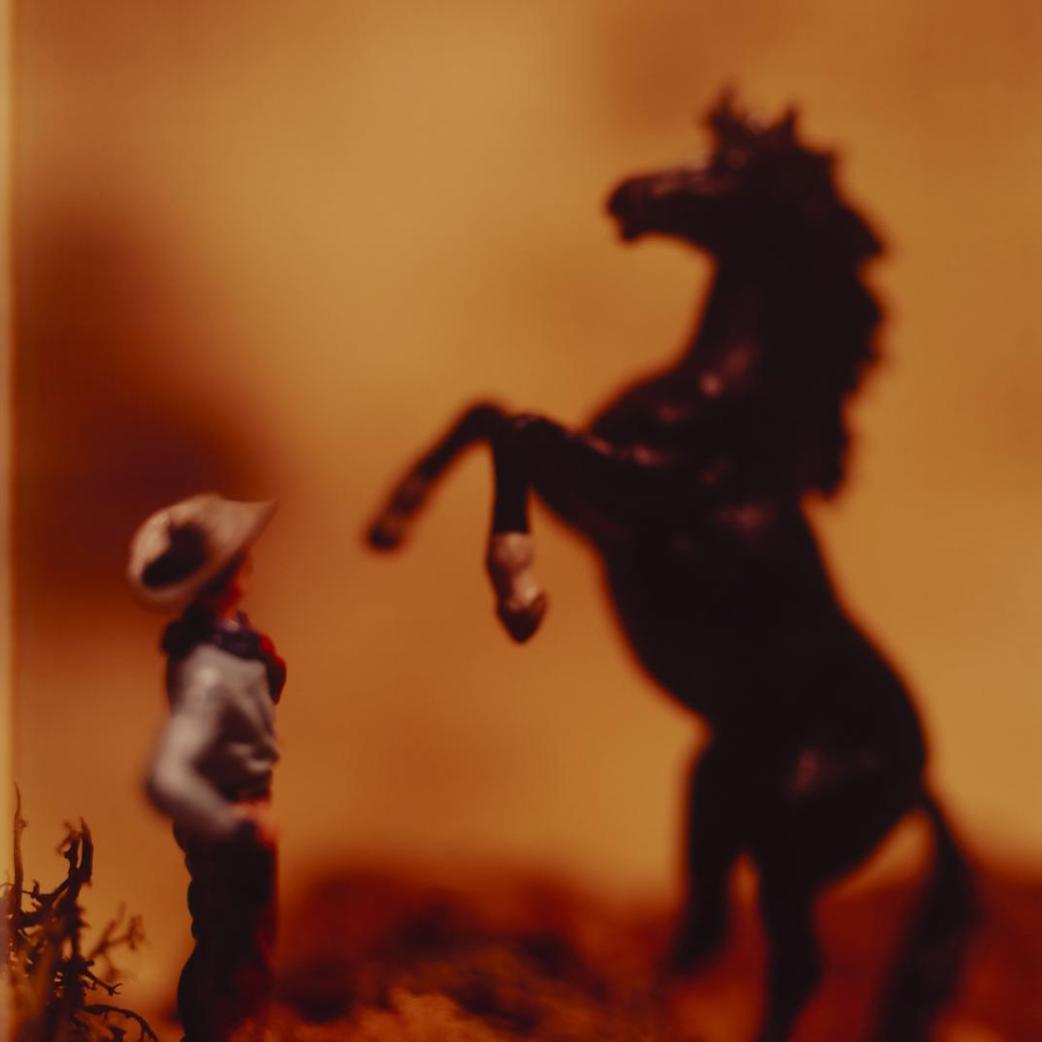 Slightly out of focus photo of a toy coboy in front of a toy horse standing on it's hind legs.