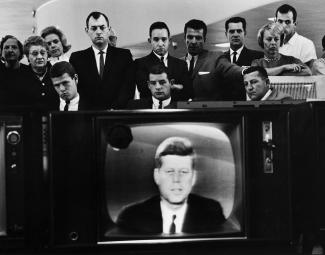 Group of people around a television set showing JFK on the screen