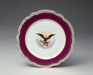 An image of a porcelain dinner plate with a maroon outer circle and white middle with eagle.