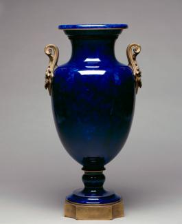 An image of a porcelain and gilded metal vase that's dark blue with brass handles. 