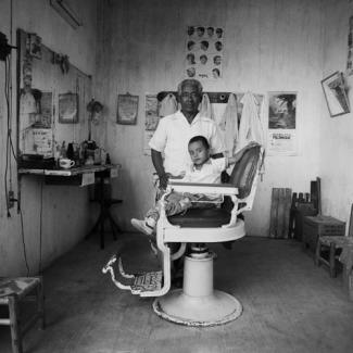Gleaton's gelatin silver print of a little boy in a salon chair posing with his barber.