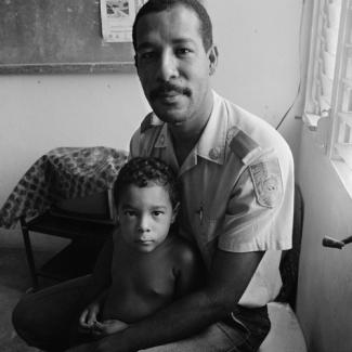 A gelatin silver print of a man and his child sitting in a room.