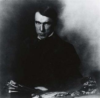 A black and white photograph of a man sitting down with paint brushes in his hand.