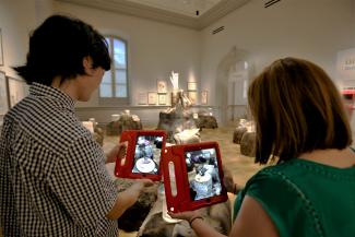A photograph of two people holding Ipads with artwork on them.
