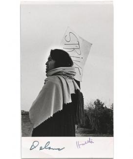 A photograph of a woman holding a protest sign with a scarf. 