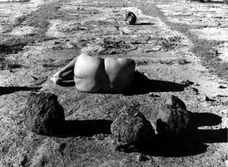 Black and white photograph of woman laying on desert ground with her backside facing the viewer