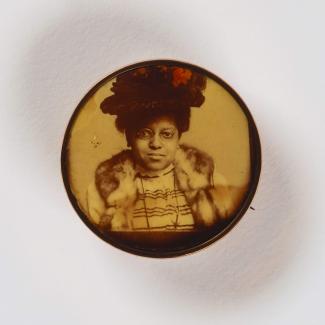 A jewelry pin showing woman in a large black hat staring directly 