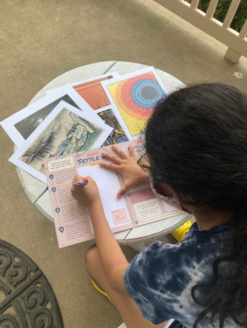 A young student sitting at a desk works their way through printed activities from the Smithsonian American Art Museum.