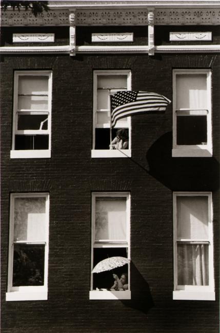 A black and white photograph of two people looking out an apartment facade.