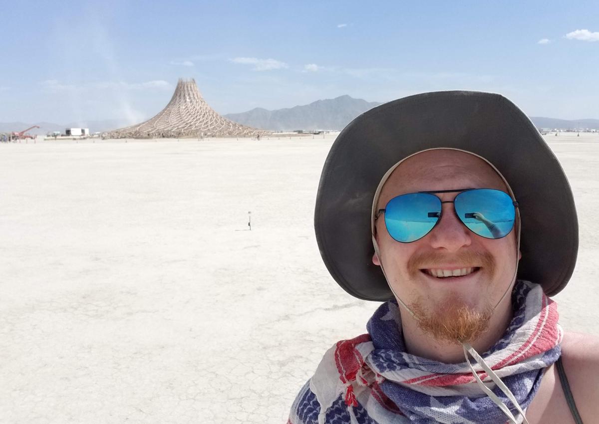 A man with sunglasses and a hat on and a structure in the background.