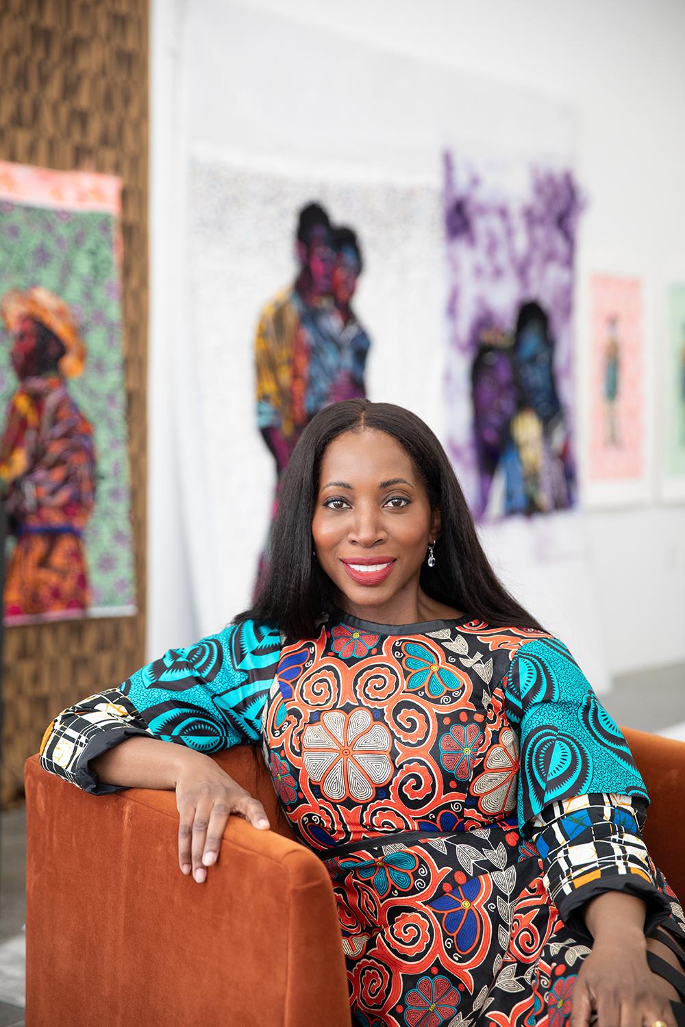 Bisa Butler sitting on a chair with her artwork behind her.