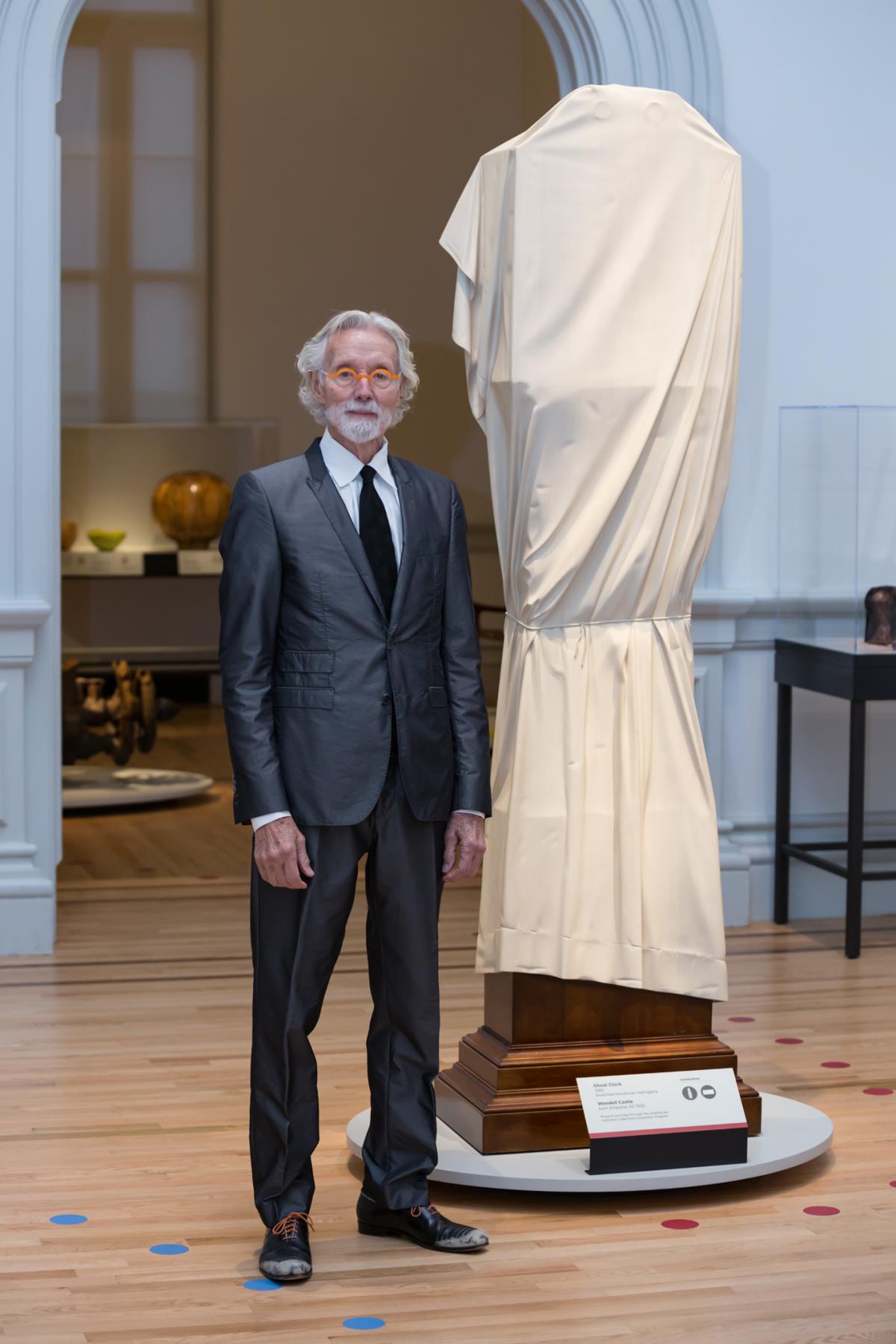 This is a photo inside the Renwick Gallery of artist Wendell Castle standing next to "Ghost Clock"