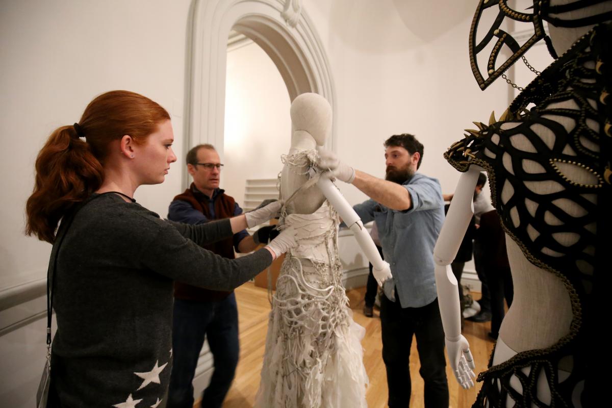 A behind the scenes shot of workers putting the costume on a mannequin
