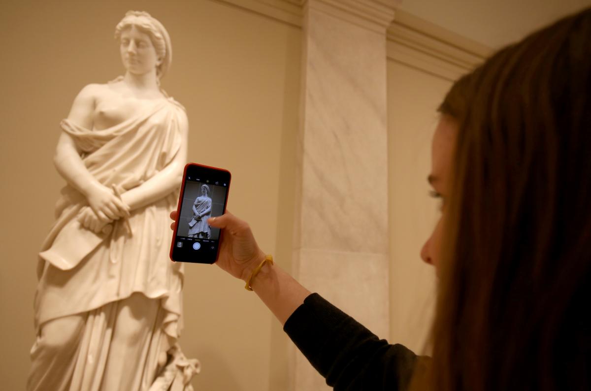 An image of a visitor taking a picture of the sculpture "Sappho" by Vinnie Ream. 