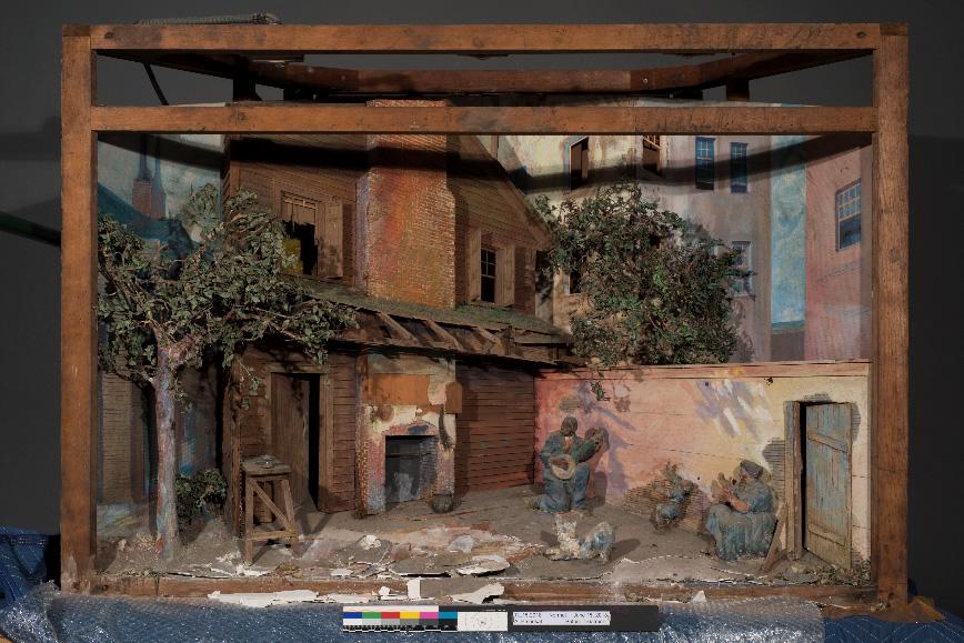 This is a photograph of a diorama with a house and man playing guitar outside with his family.