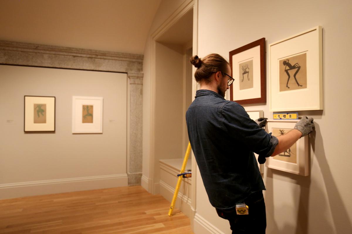 Photo of a man hanging pictures on a gallery wall and checking them with a level.
