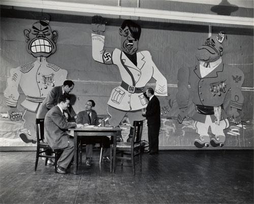 An image of men sitting at a table talking with a mural behind them.