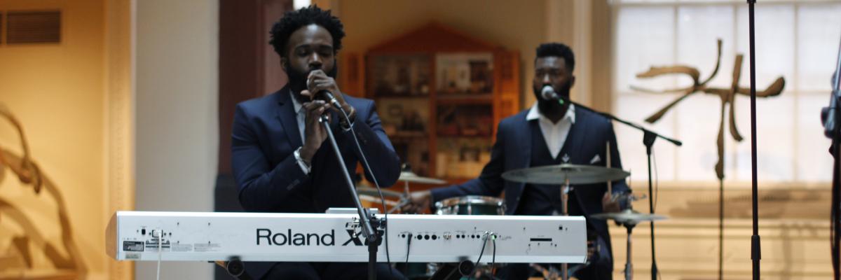 A man playing at a piano and a drummer behind him.