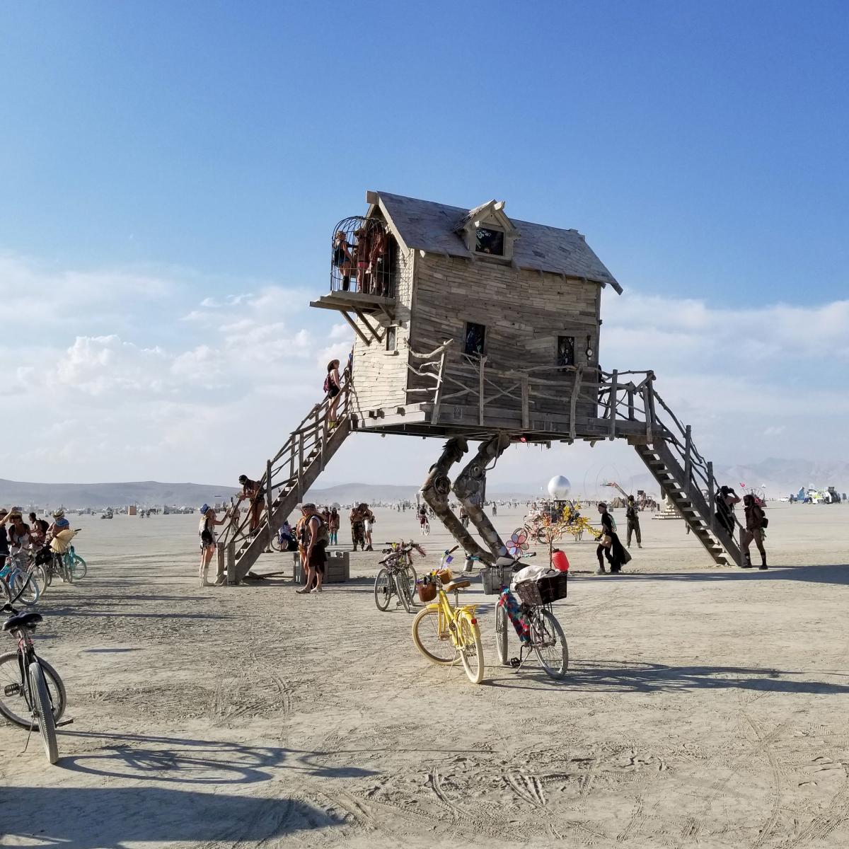 A photograph of a house with robot legs in the desert. 