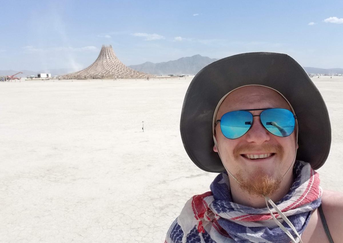A man with sunglasses and a hat on and a structure in the background.
