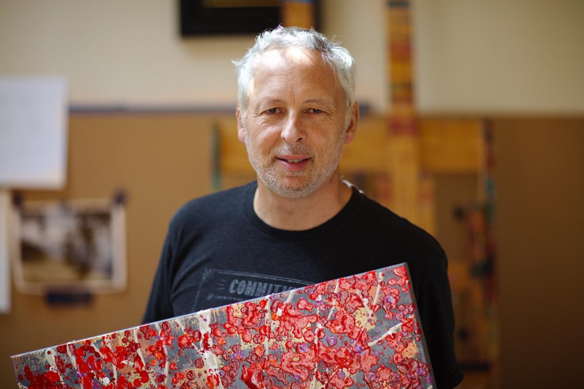 A photograph of a man holding a red painting. 