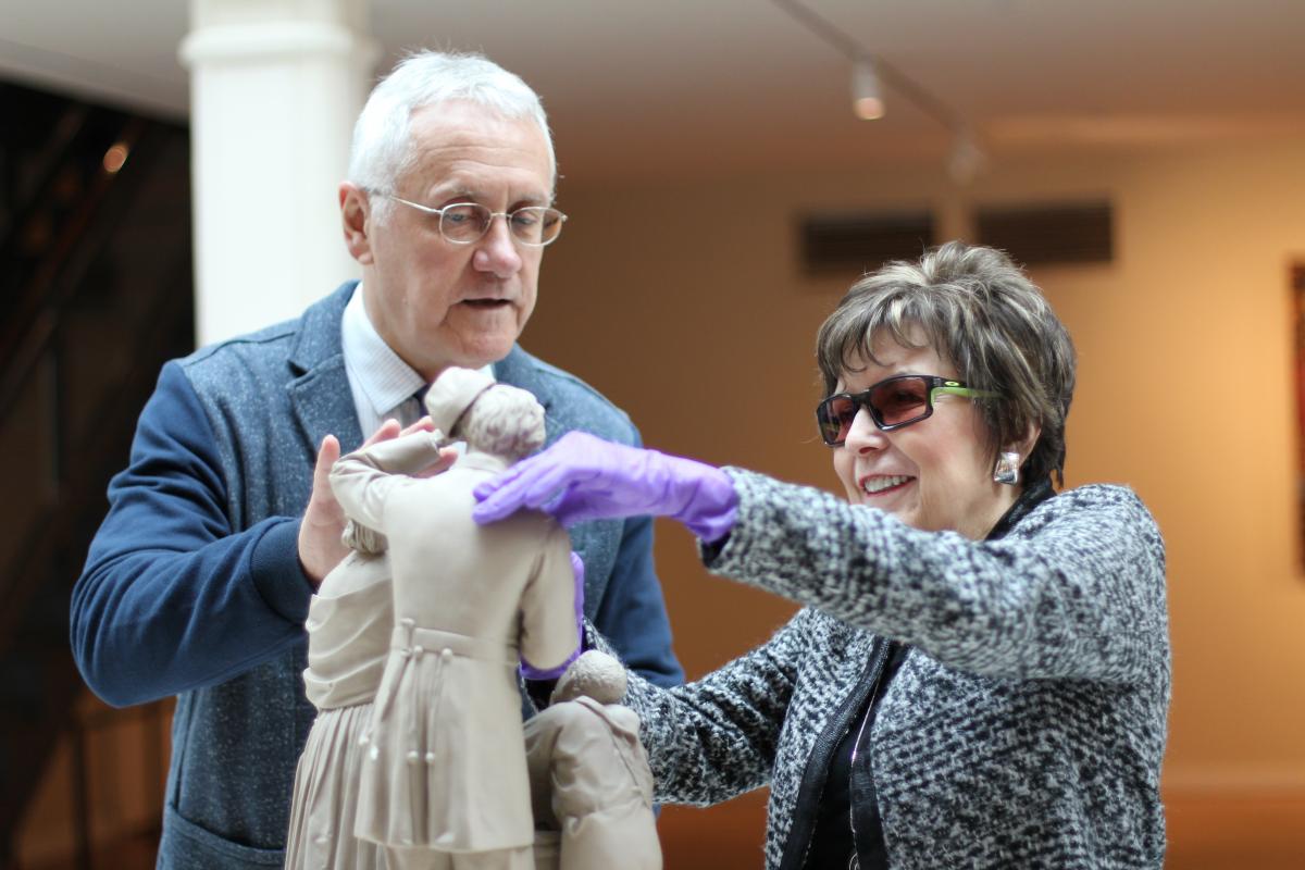 A photograph taken inside the museum of a blind lady with gloves touching a replica of a sculpture.