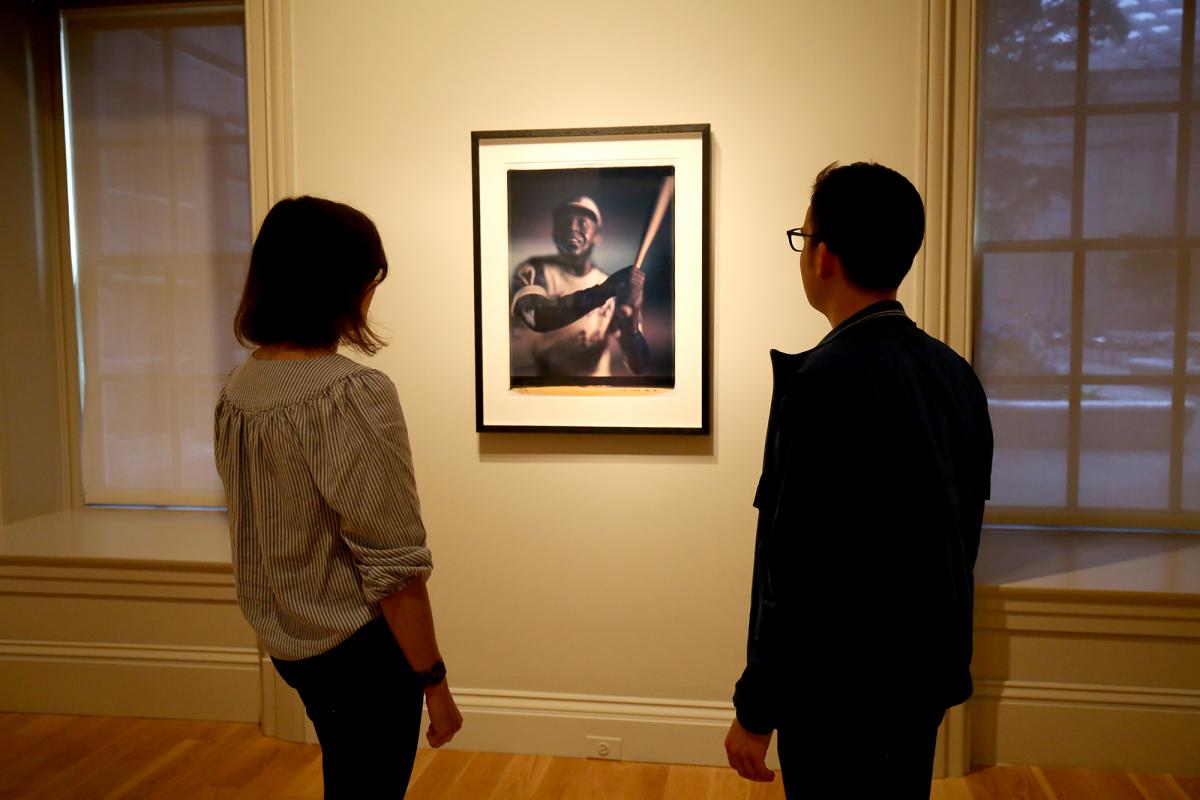 A photograph of two people looking at a piece of artwork on a wall.