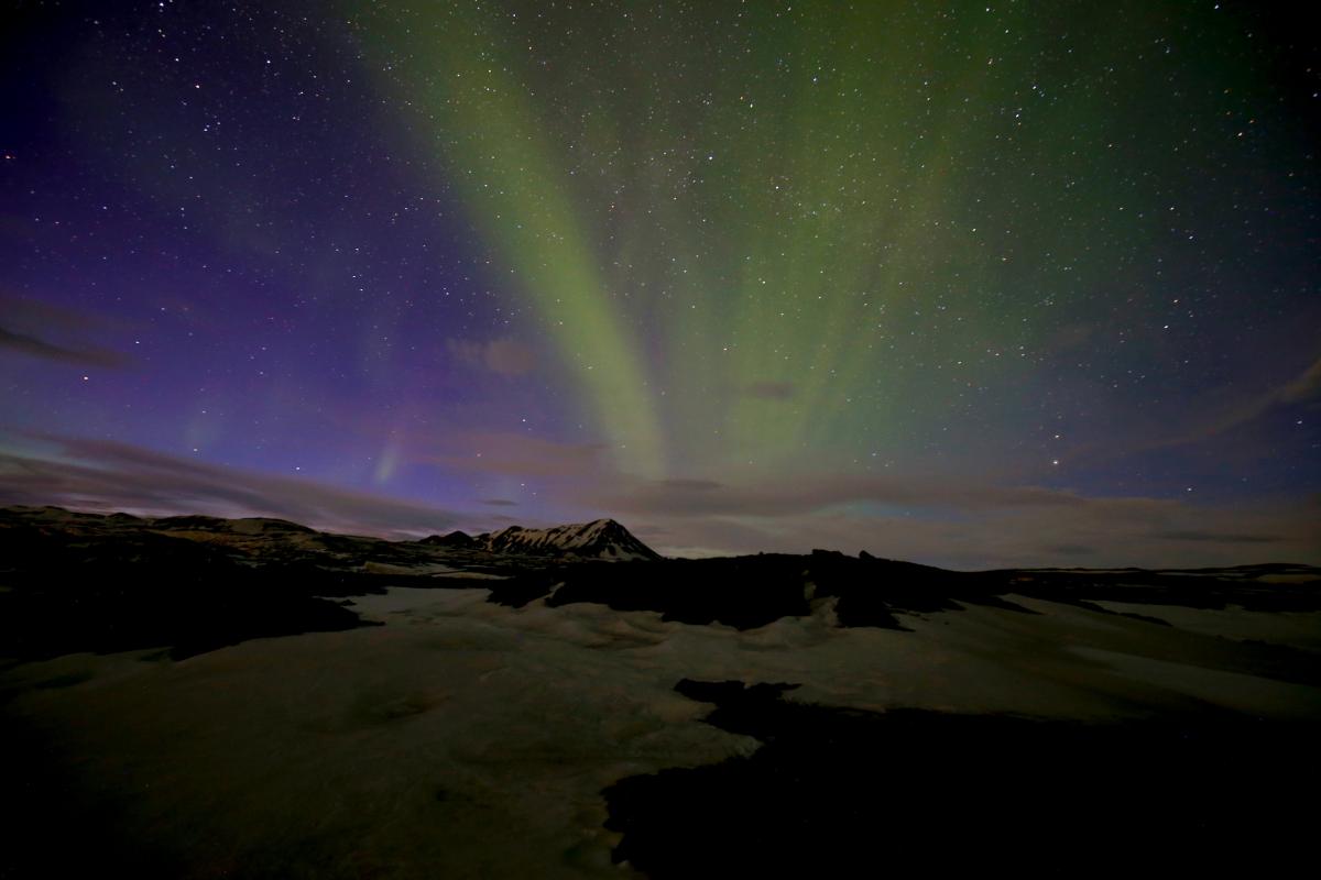 A photograph of a mountain with green northern lights overhead. 