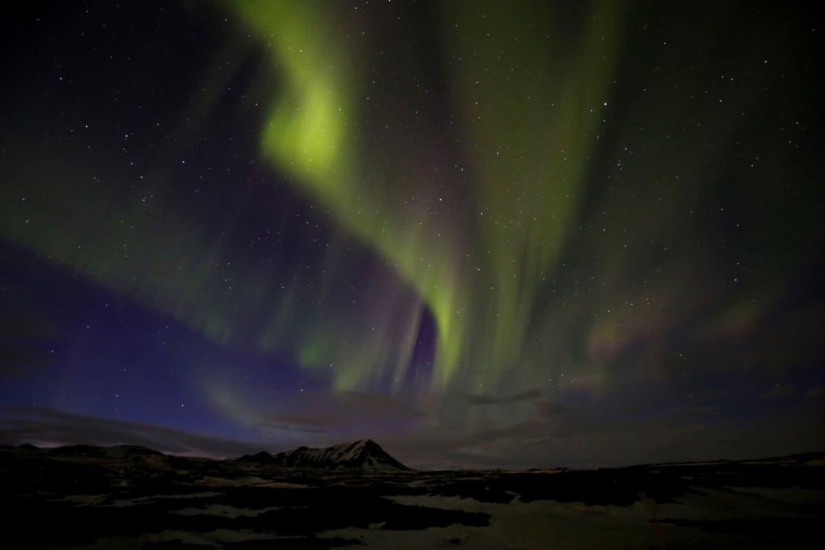 A photograph of a mountain with green northern lights overhead. 