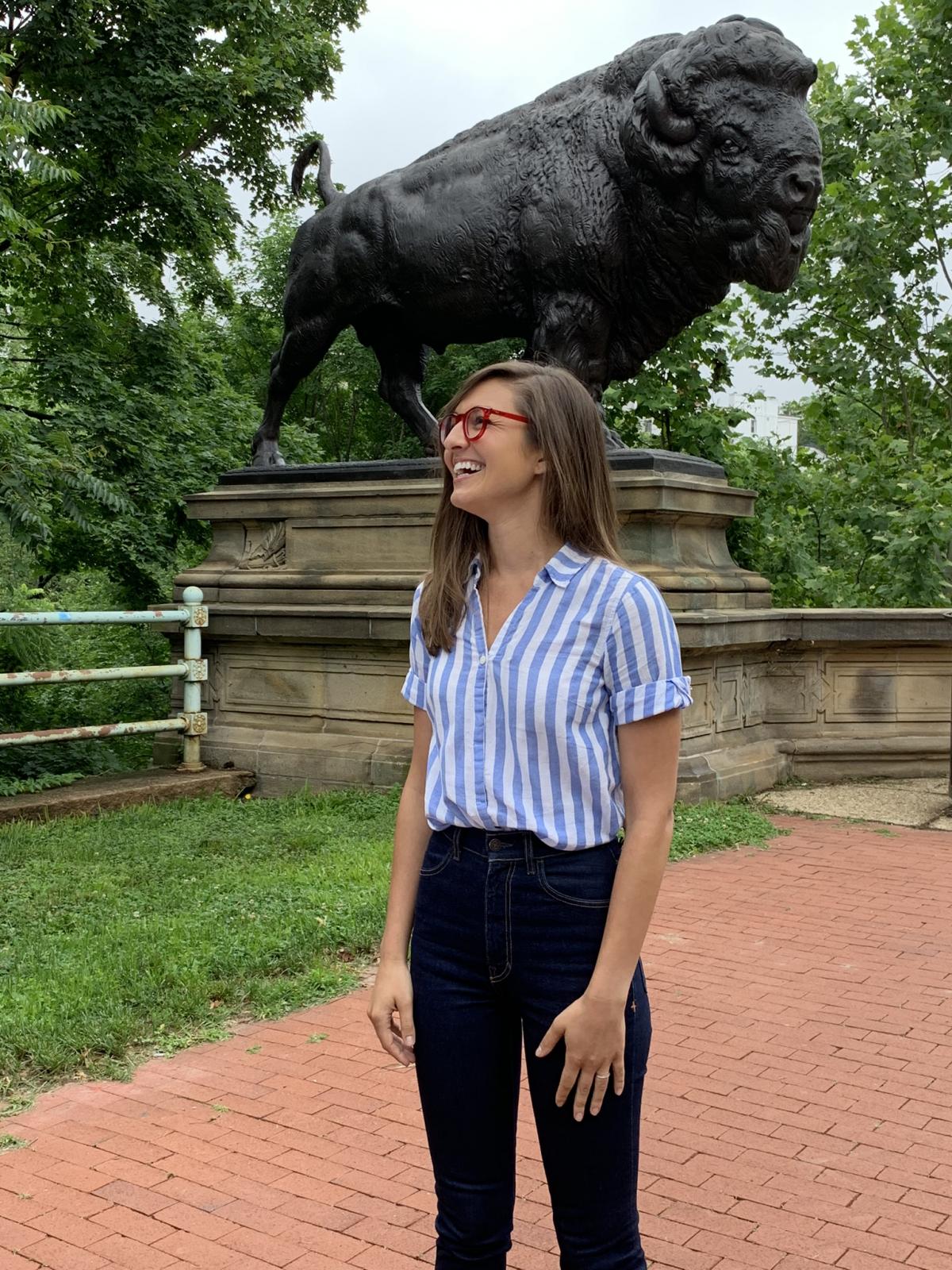 A photograph of a woman standing in front of a sculpture of a bison