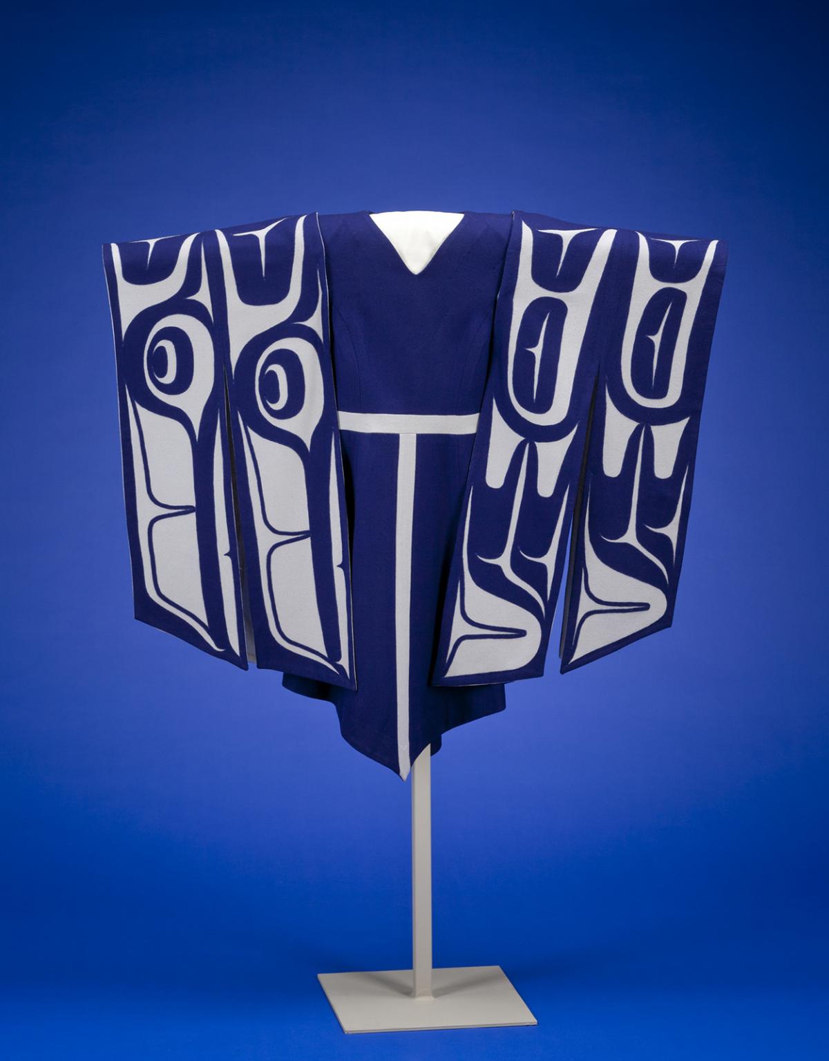 A blue dress handing on a stand with sleeves made of white and blue material depicting wings.