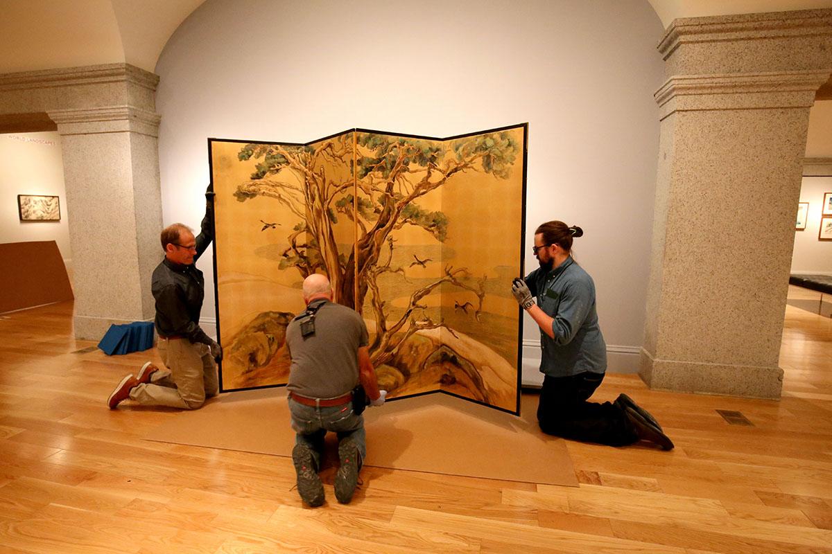 Three men installing a silk screen. 