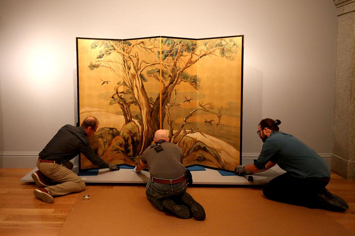 Three men installing a silk screen. 