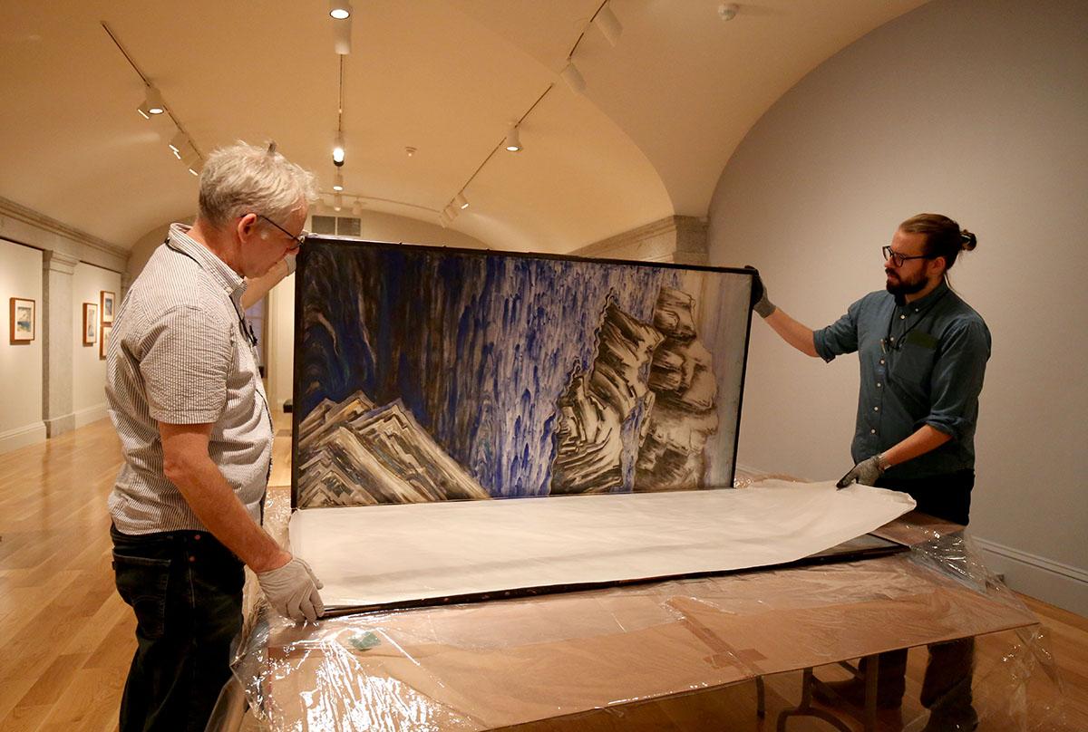 A photograph of two men unpacking a silk screen.