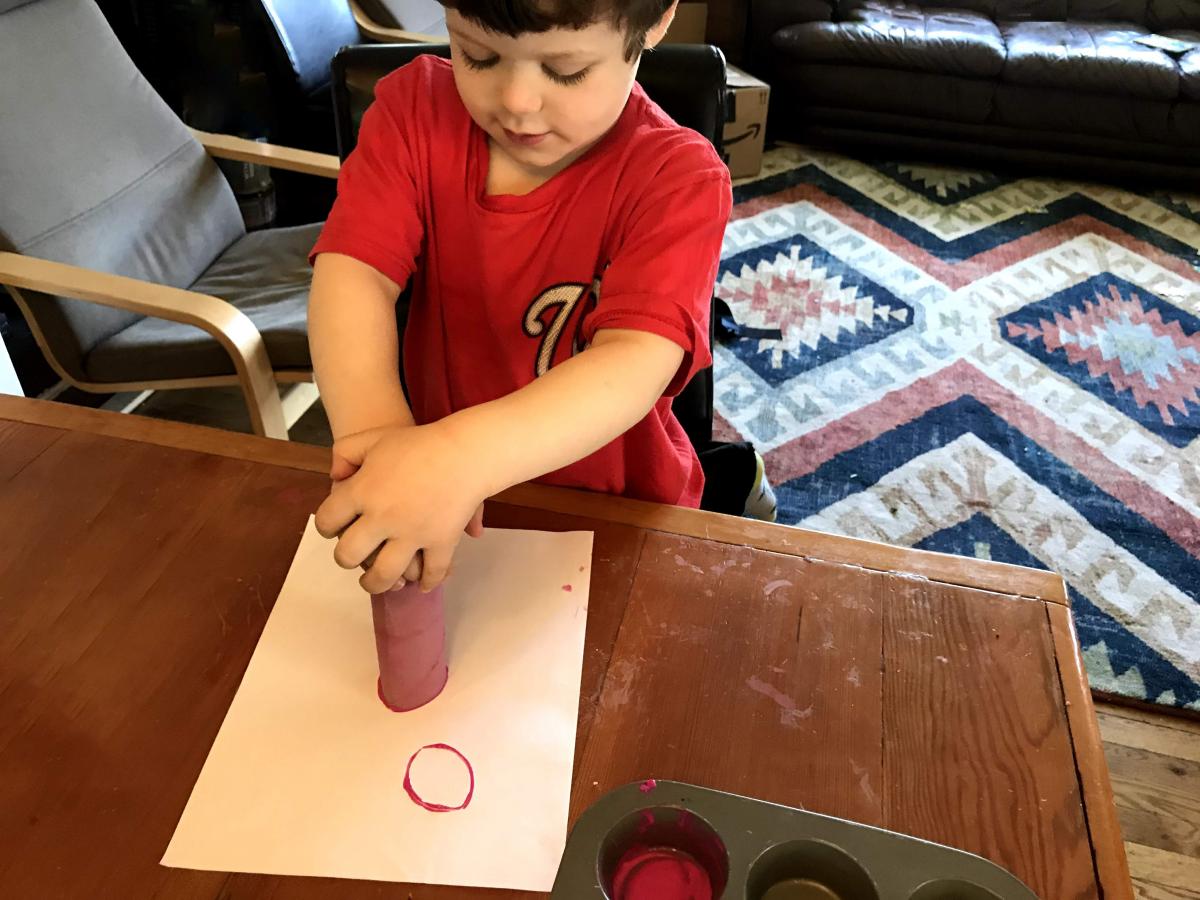 A photograph of a child making a stamp flower with a paper towel roll. 