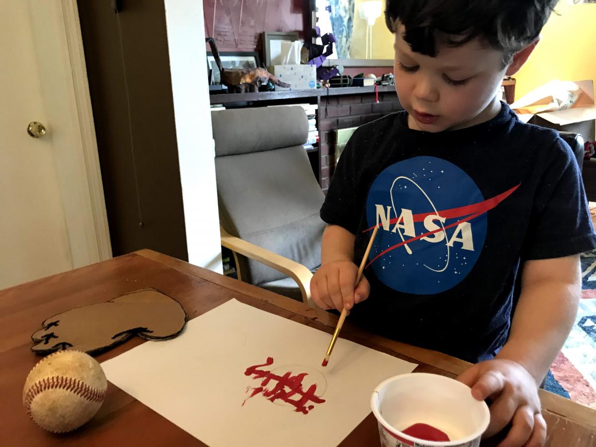 A photograph of a child painting on a piece of paper. 