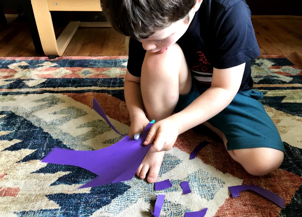 A photograph of a young child cutting purple construction paper. 