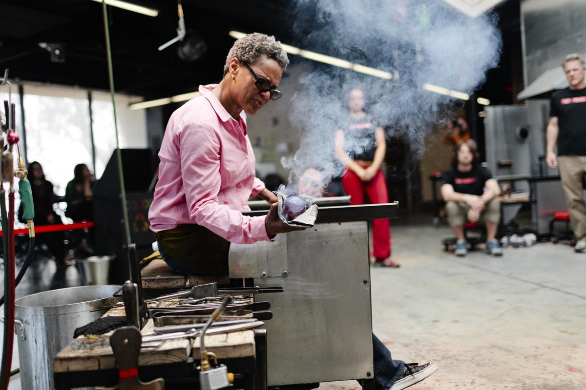 A photograph of a woman in a studio blowing glass. 