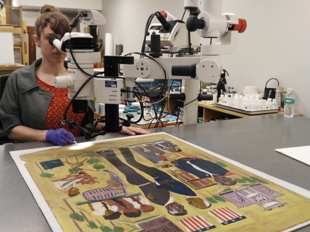 Intern looking through a microscope while treating a painting