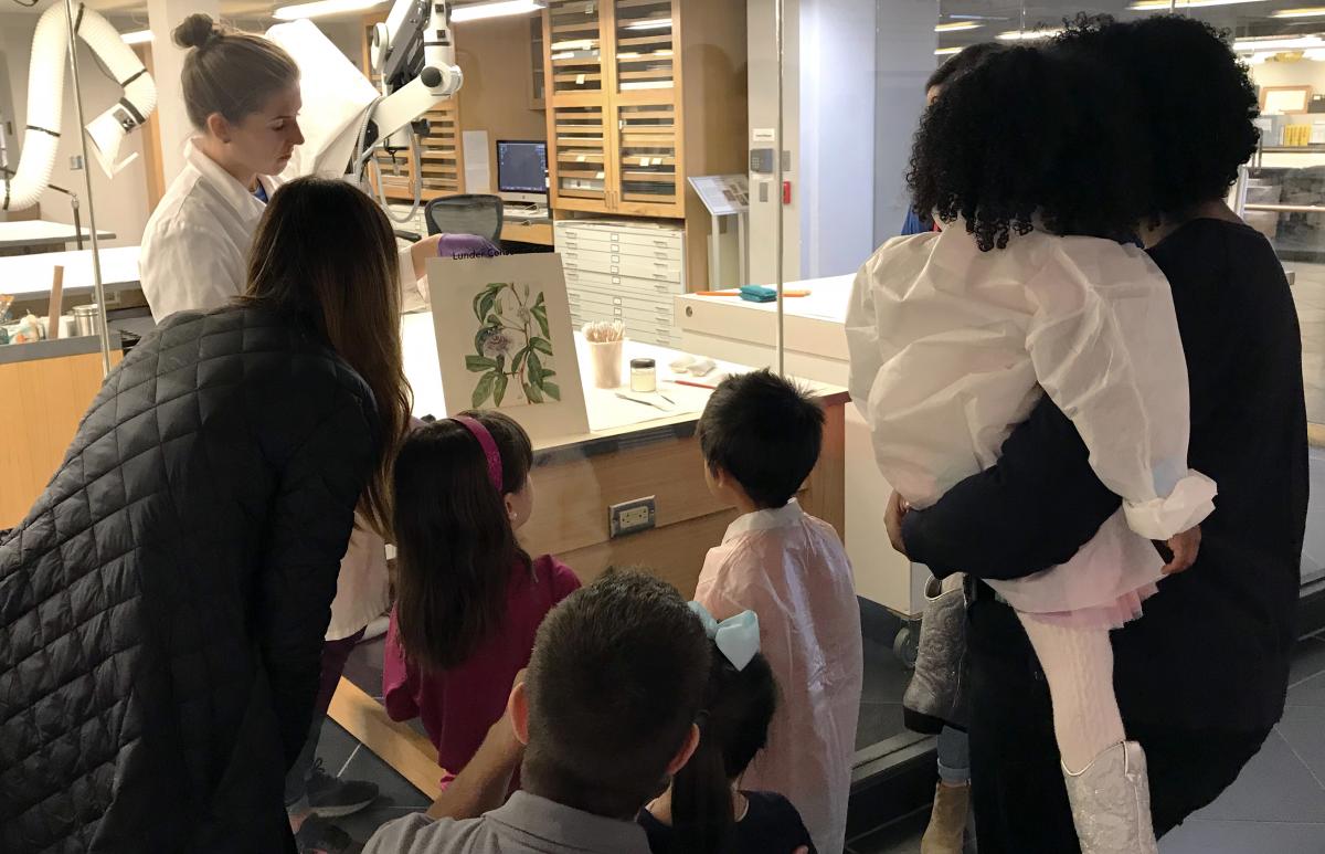 A photo of a family looking through glass at a conservator at work.