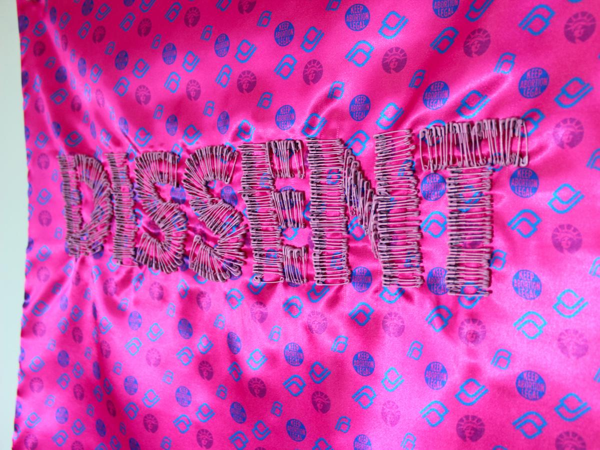 A photograph of material with the word "dissent" stitched into it