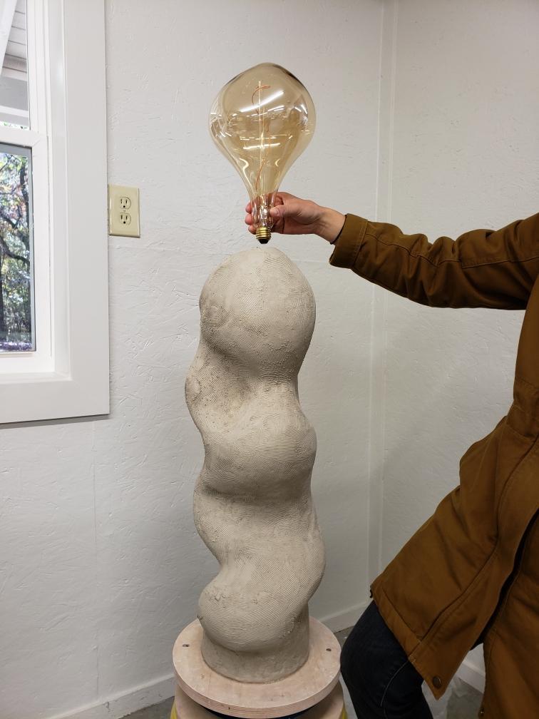 A photograph of a sculpture with a light bulb at the top