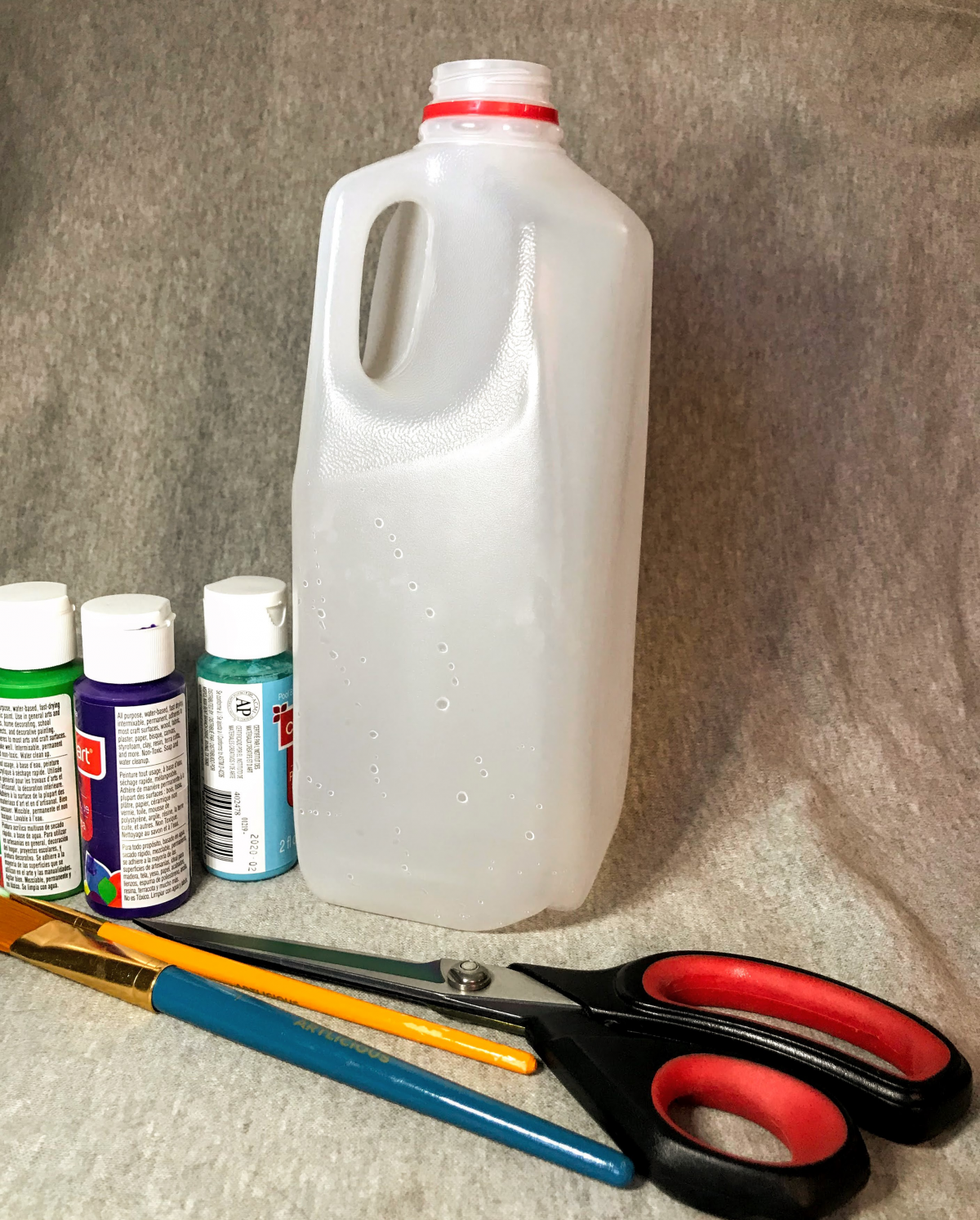 A grouping of supplies: milk jug, paint, and scissors
