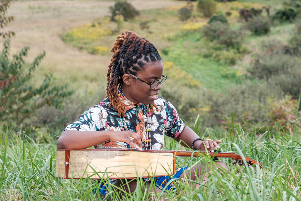 photo of Yasmin Williams playing guitar while sitting in the grass