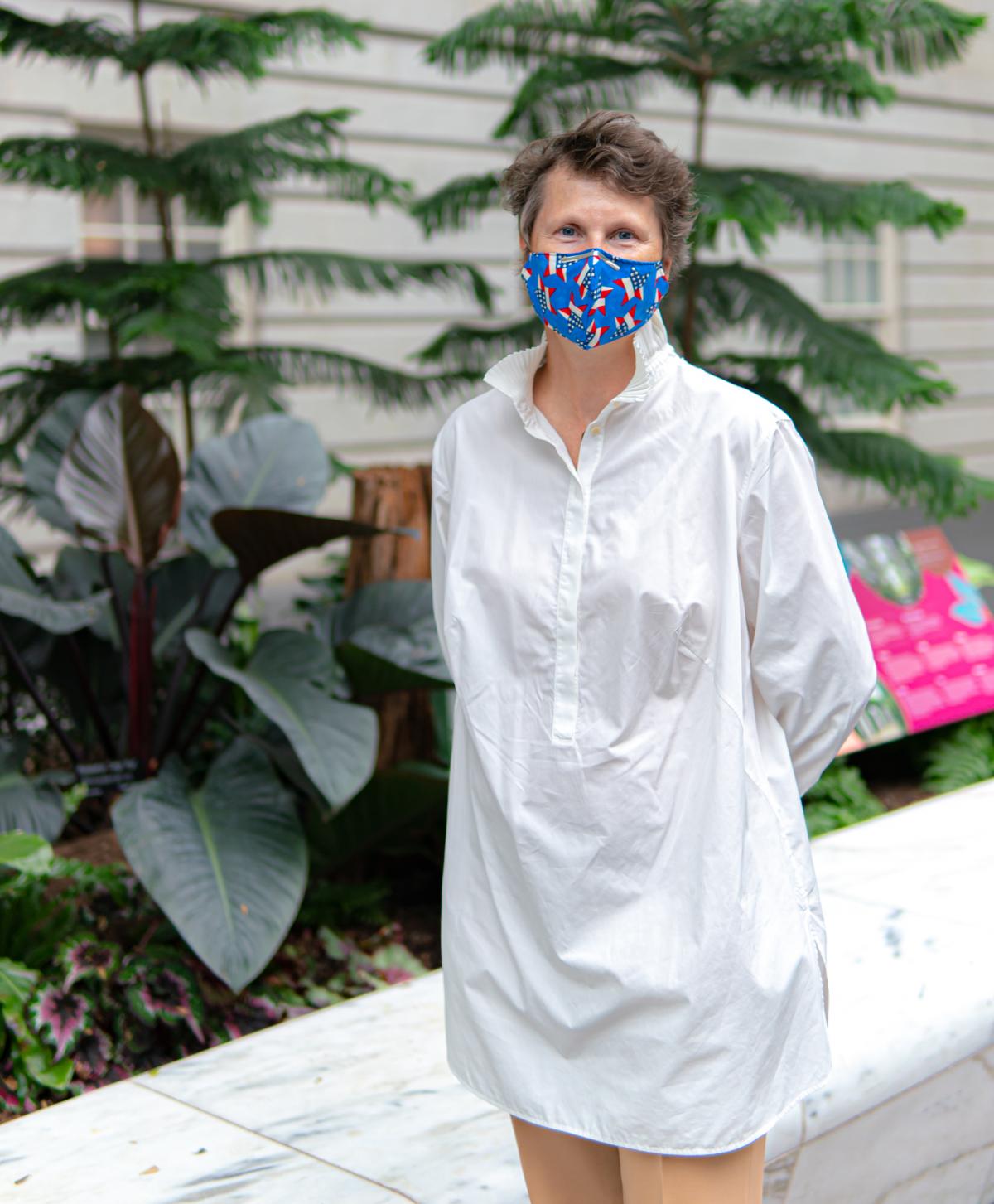 A woman in a blue mask standing in front of plants.