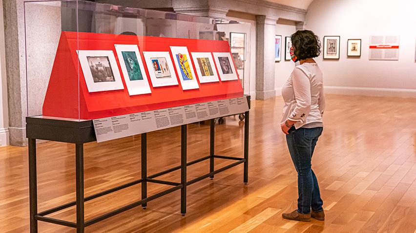 A person with short hair stands in front of a case of prints.