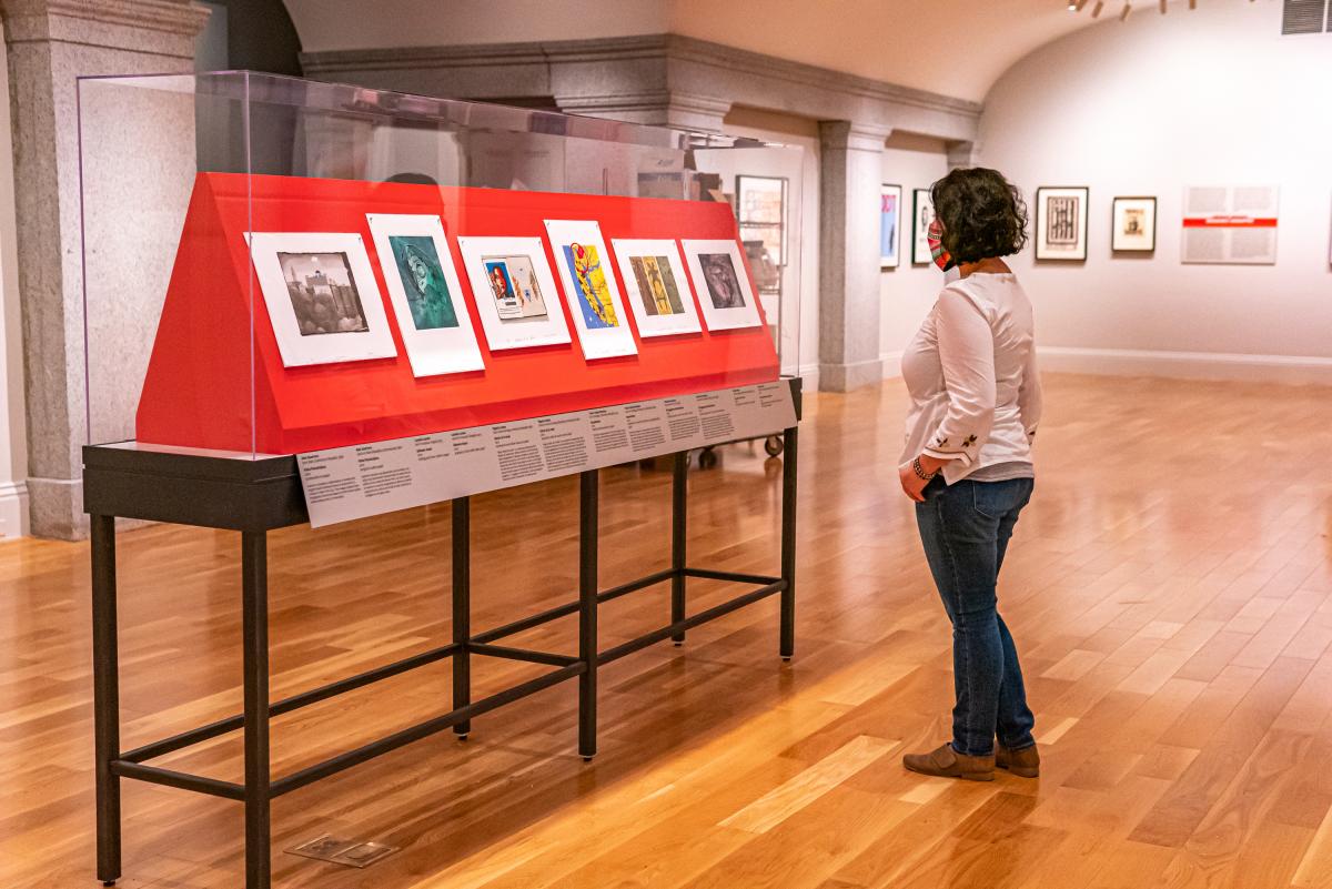 A person with short hair stands in front of a case of prints.