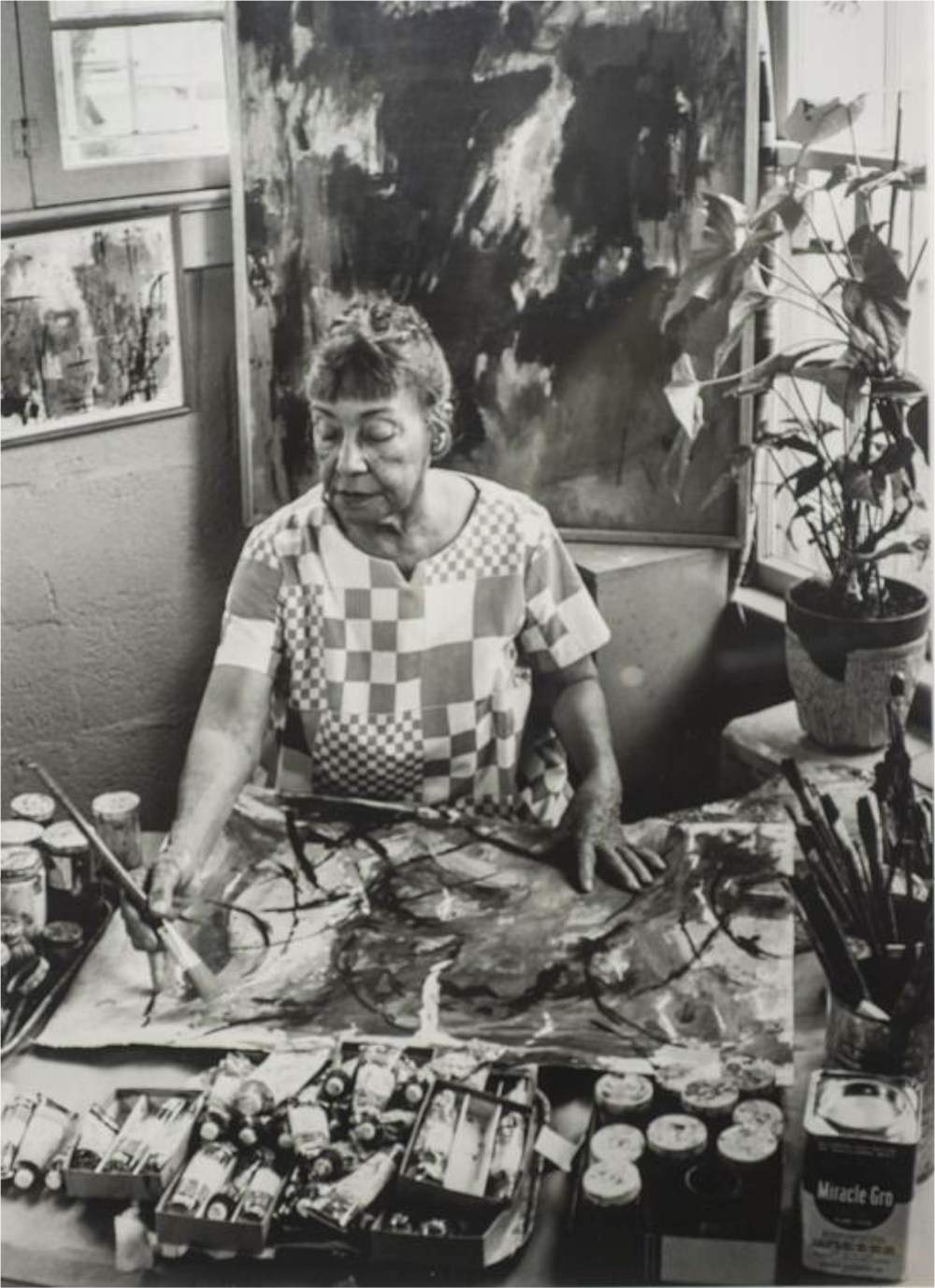 A black and white photograph of artist Alma Thomas painting in her studio.